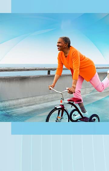 Happy middle aged woman riding a bicycle in the beach front free from ostomy care problems